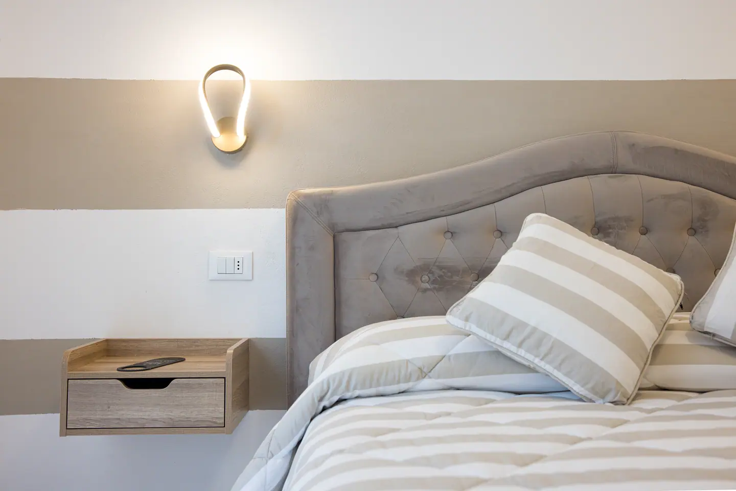 Dettaglio della testiera capitonné con applique accesa e comodino in rovere