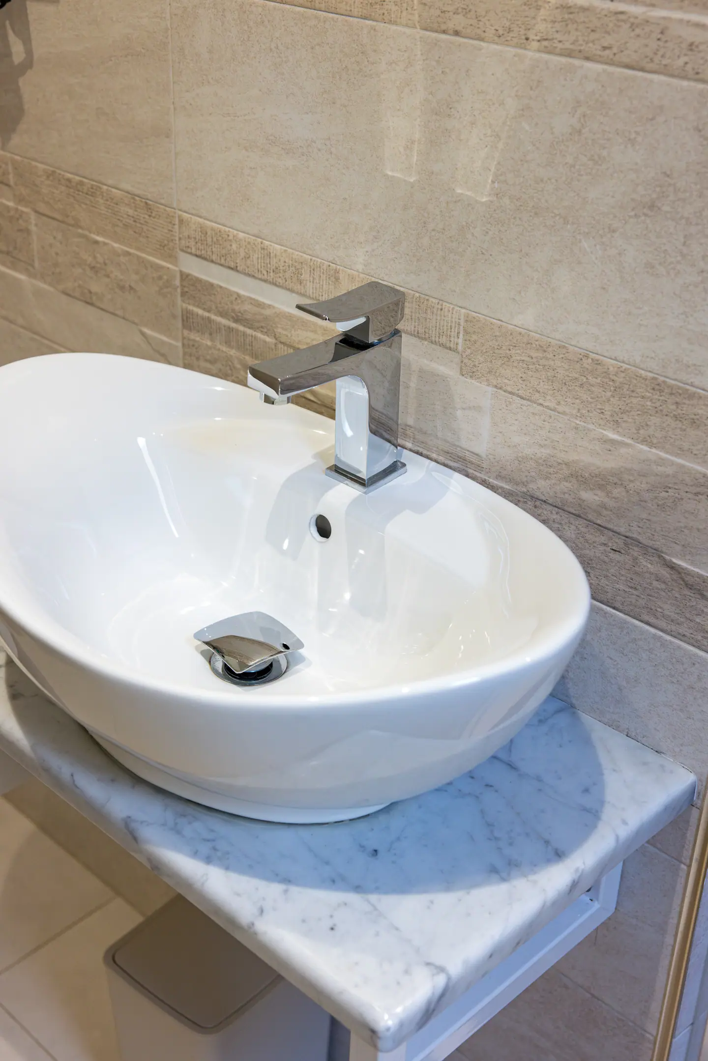 Lavabo ovale su mensola in marmo di Carrara contro piastrelle in travertino