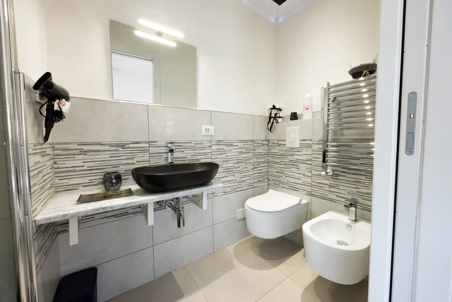 Il bagno privato con lavabo ovale nero opaco e termoarredo cromato