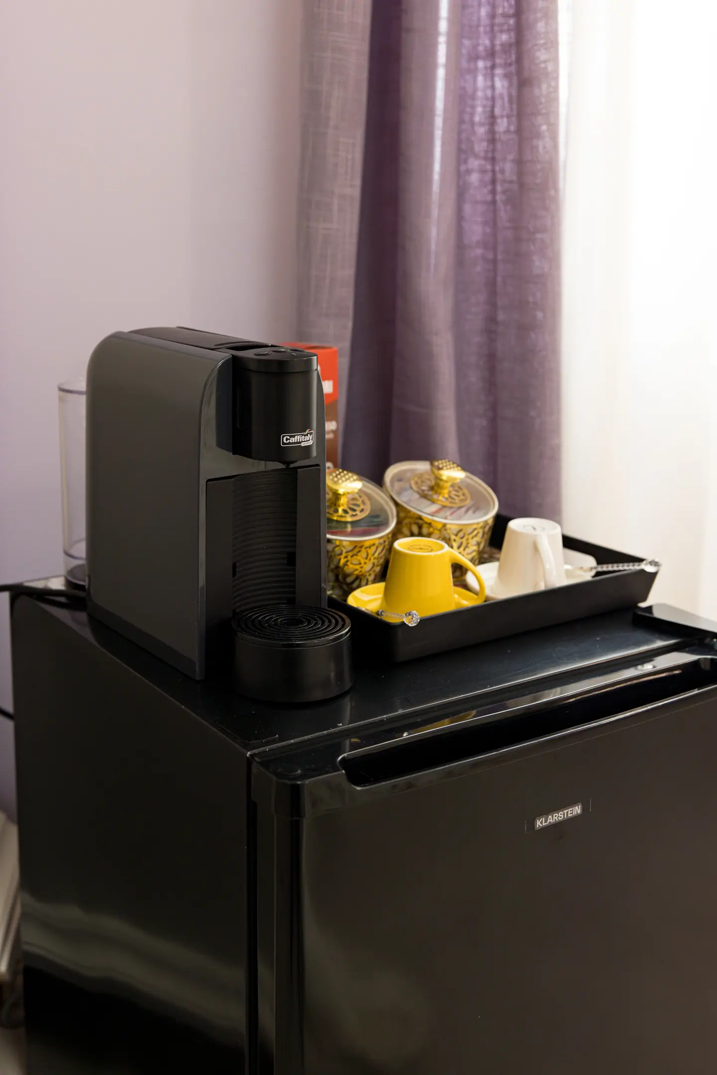 Macchina da caffè e minibar in camera, con tende viola alla finestra